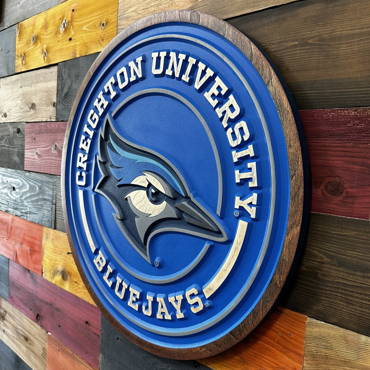 Creighton University Bluejays logo on a wooden plaque against a multicolored wood panel background