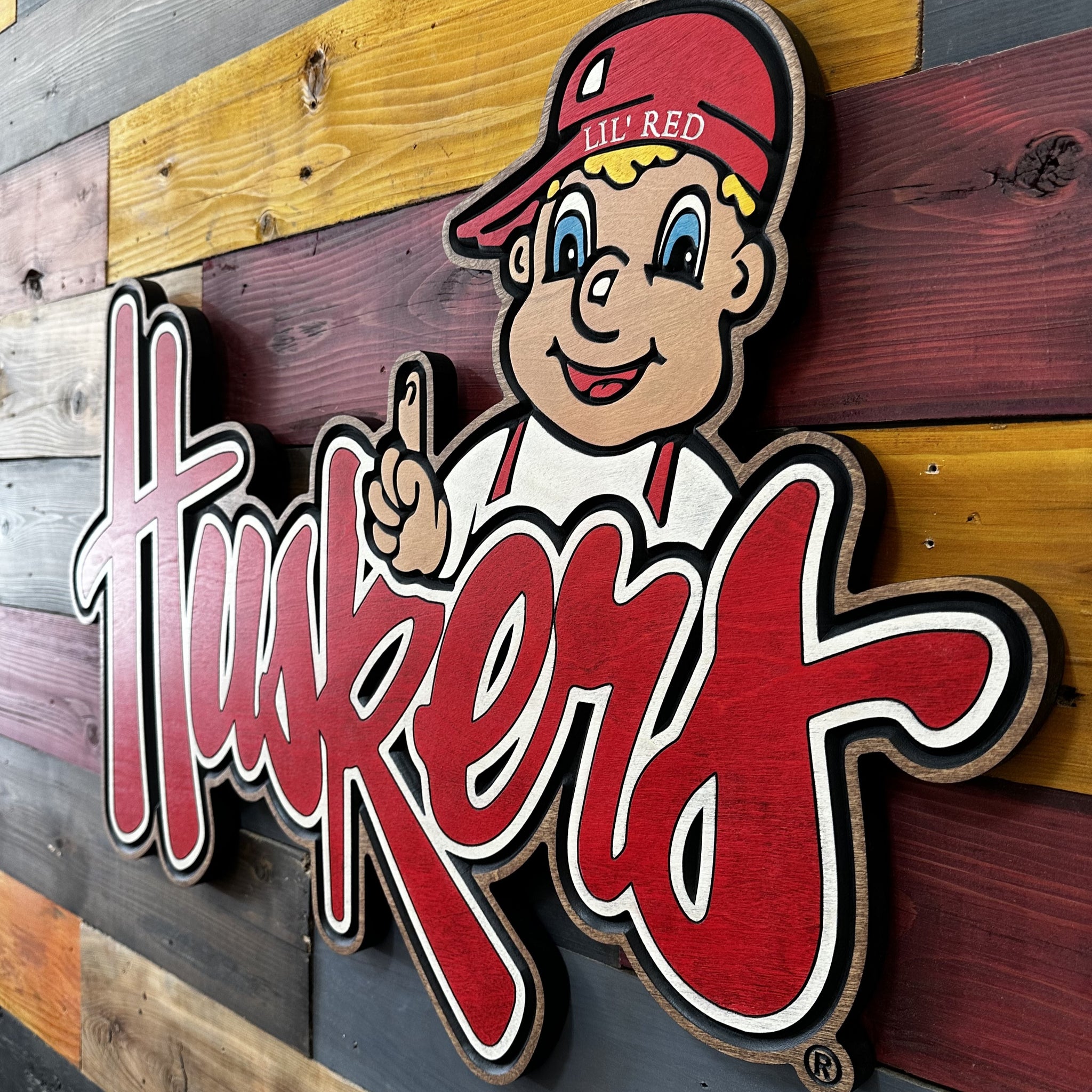 Lil’ Red cursive Huskers sports wood art displayed on wall
